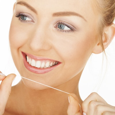 Headshot of a woman holding a piece of floss to show the importance of this activity to stop gum disease.